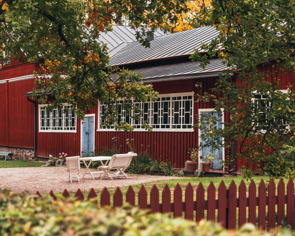 Punainen Meritalon museorakennus, jossa kuistilla pitkä rivi pieniruutuisia ikkuinoita ja kuistin edustalla puutarhan istuskeluryhmä