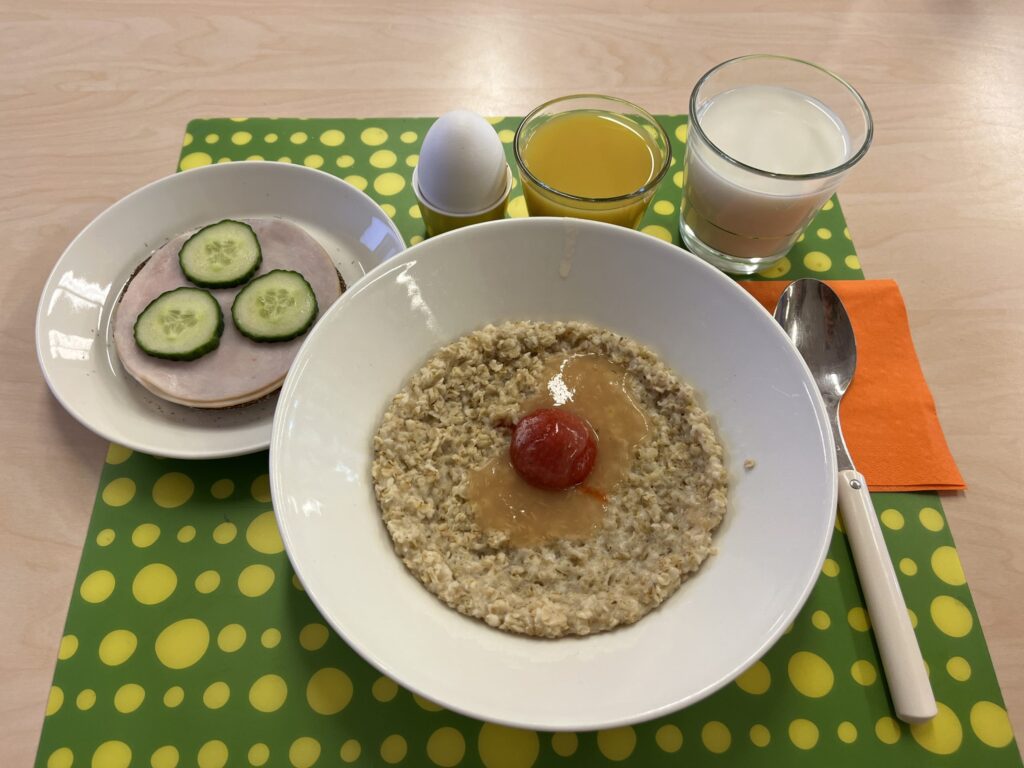 Kuvassa aamupalakattaus, jossa puuroa, voileipä, kananmuna, maitoa ja mehua.