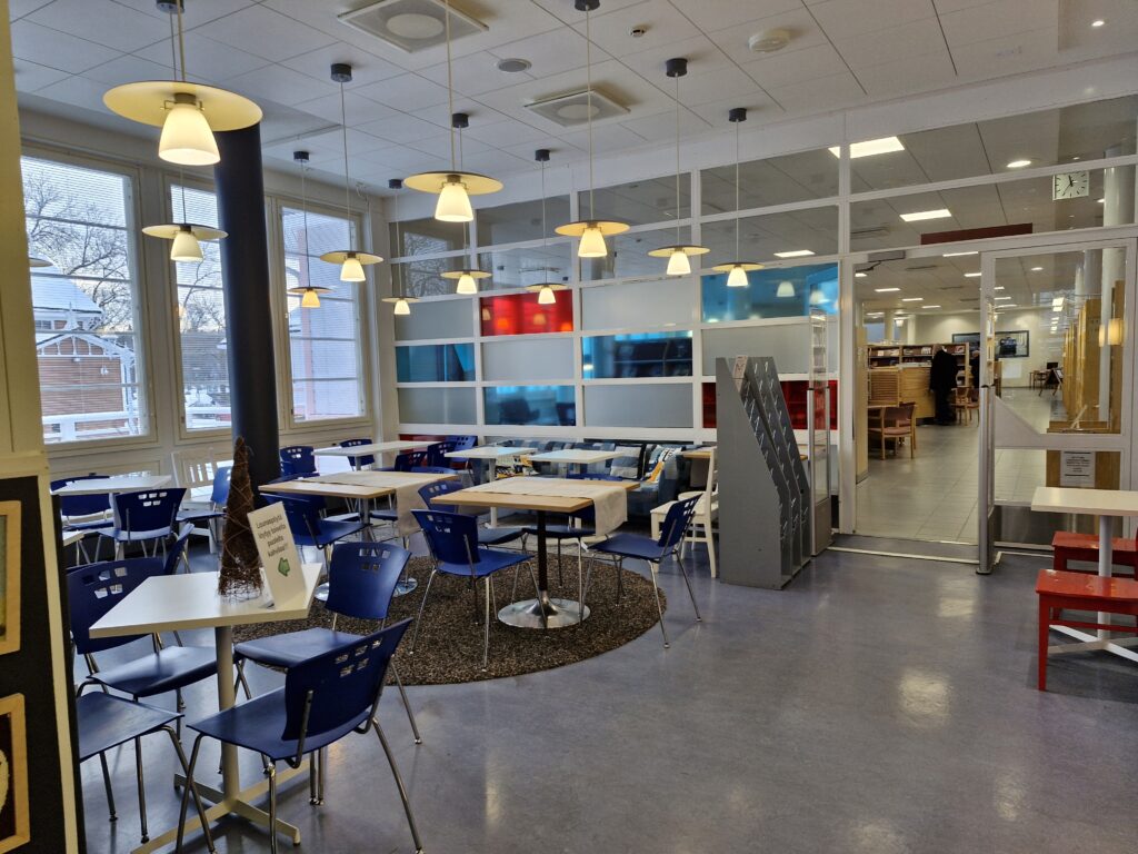 Kuva on otettu yhteisötilasta kalustuksineen, tilassa on mm. tuoleja ja pöytiä.