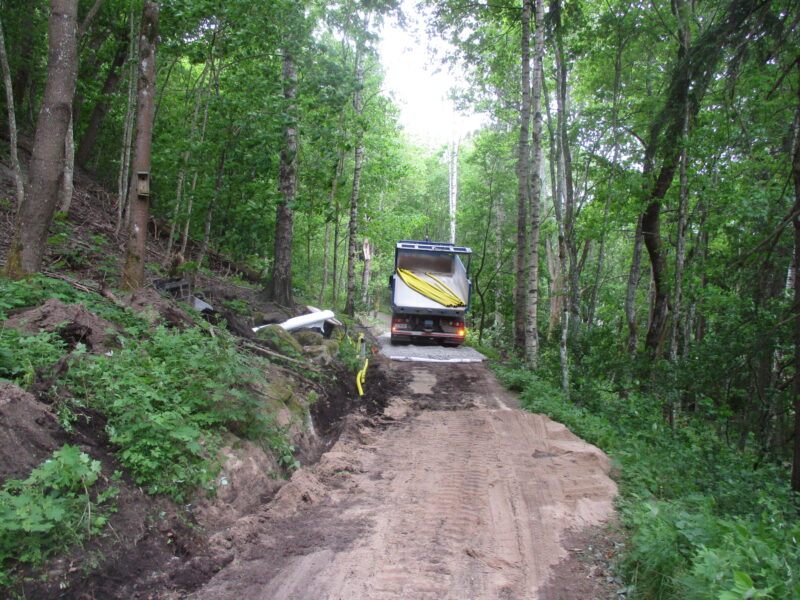Kuorma-auto levittämässä kivituhkaa metsäiselle kulkuväylälle.